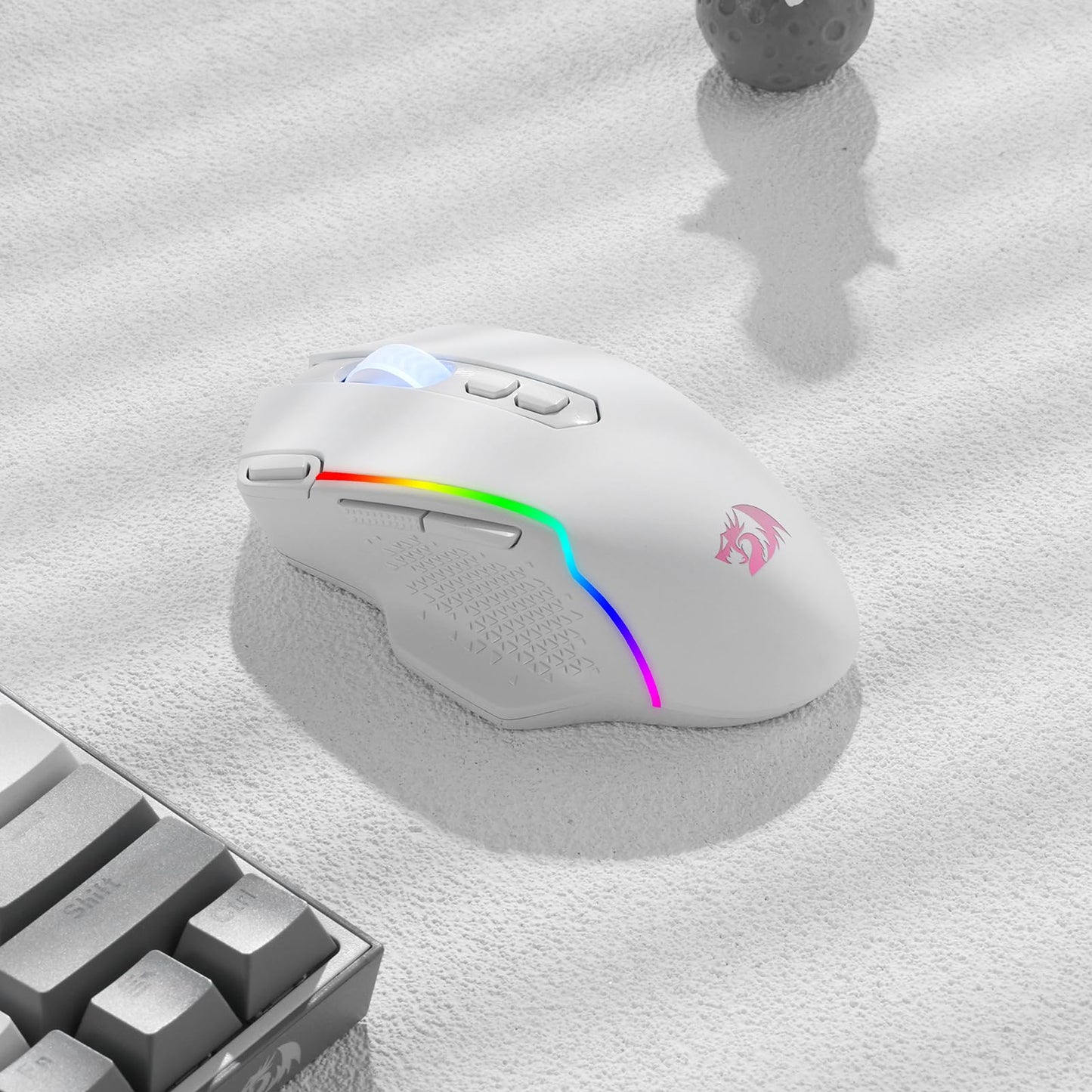 A white gaming mouse with RGB lighting on a light grey surface, next to a mechanical keyboard.