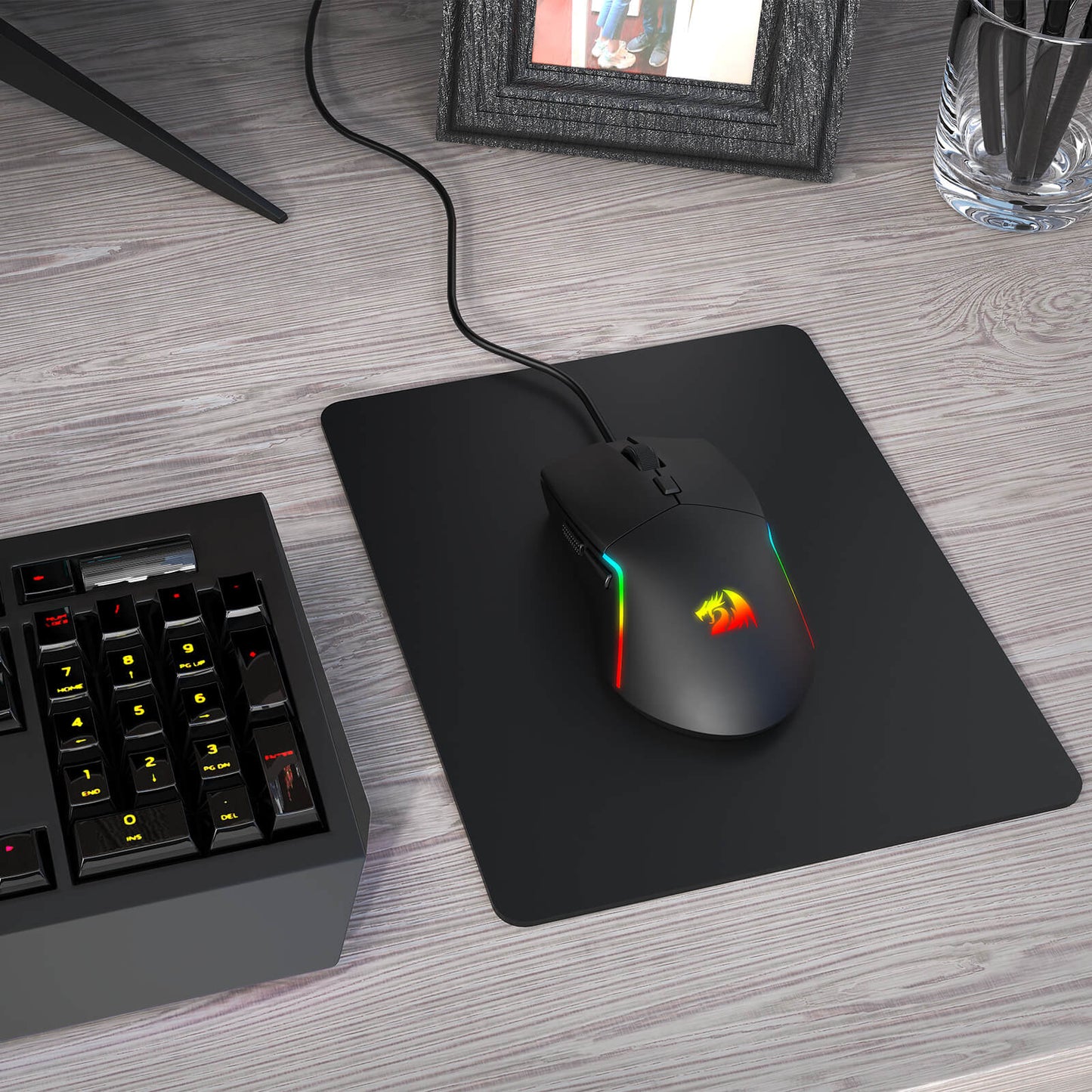 Gaming mouse with RGB lighting on a mouse pad next to a keyboard on a desk.