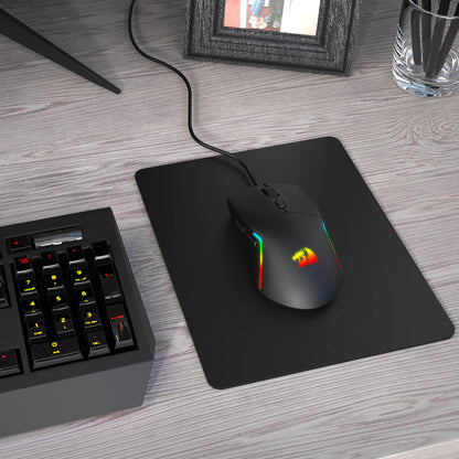 Gaming mouse with RGB lighting on a mouse pad next to a keyboard on a desk.