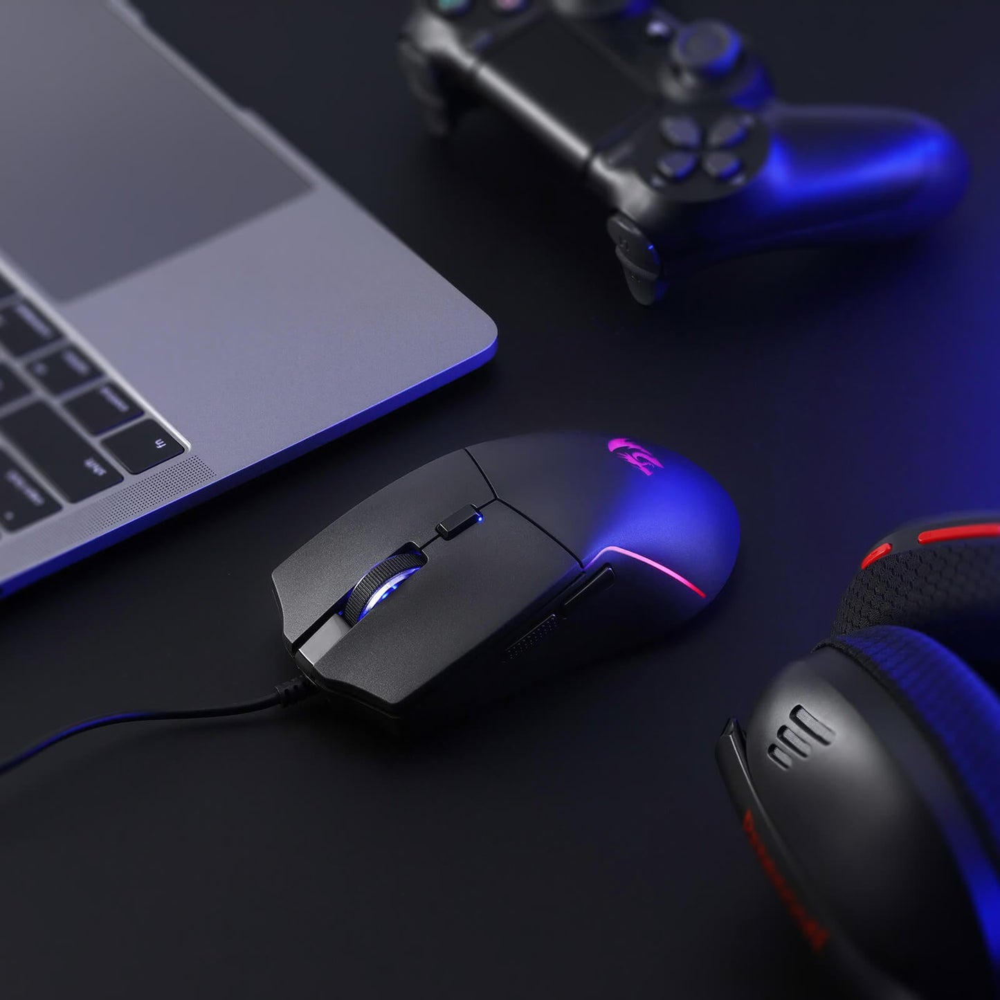 Gaming mouse and headset on a dark surface with a laptop and controller in the background