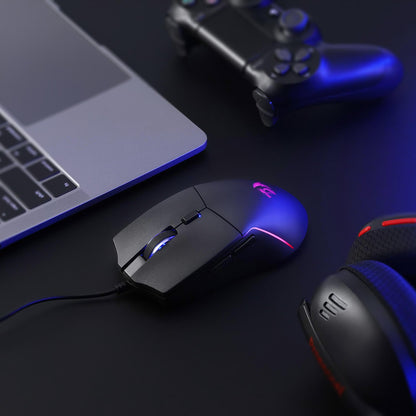 Gaming mouse and headset on a dark surface with a laptop and controller in the background